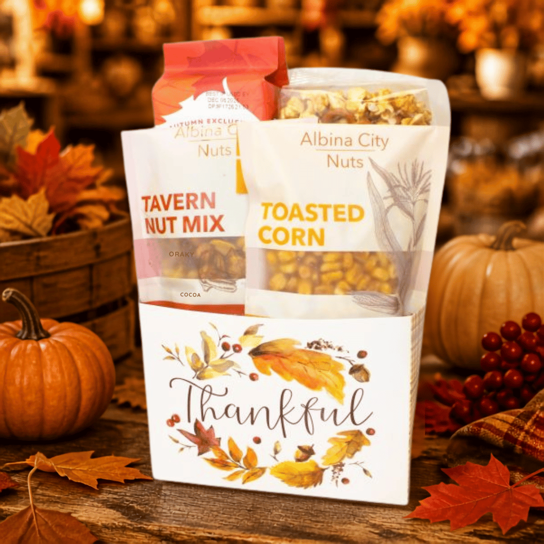 A fall-themed gift basket filled with packaged snacks, including Albina City Nuts, Tavern Nut Mix, and Toasted Corn, decorated with autumn leaves, pumpkins, and berries on a rustic wooden table.